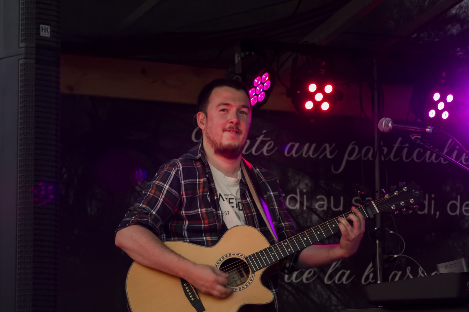 Symbiose en concert en 2026, Alex chante et joue de la guitare sur une scène illuminée